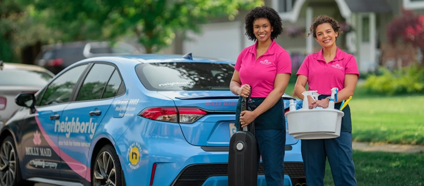Smiling Molly Maid service professionals standing near car.