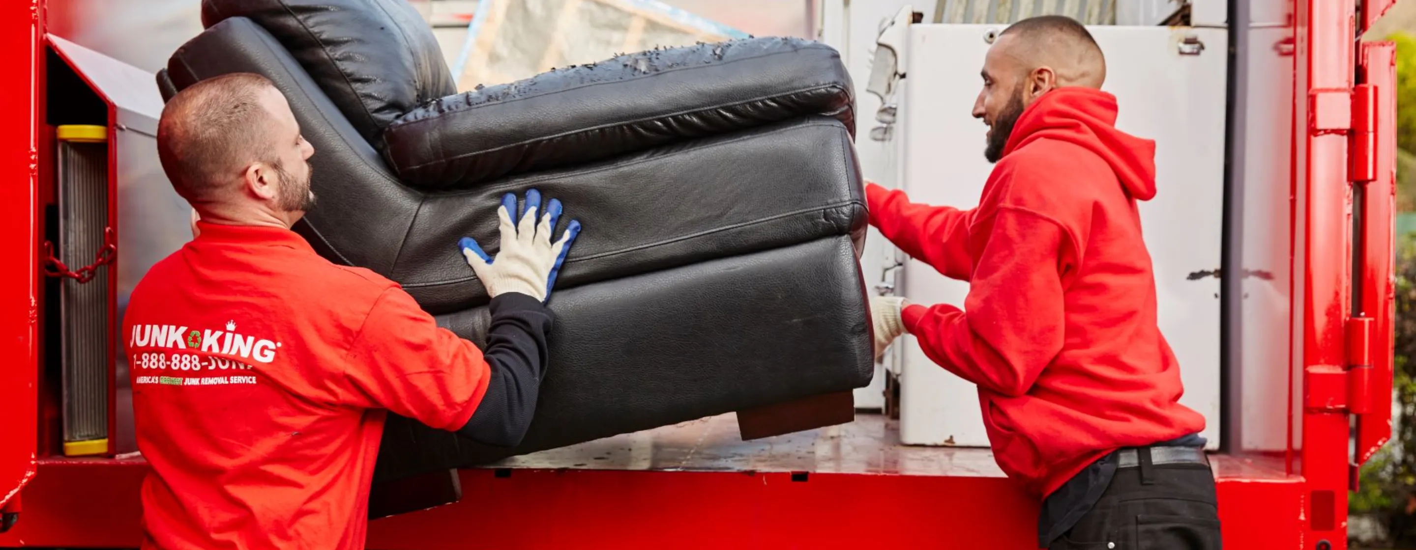 Two men lifting a sofa into a Junk King trunk