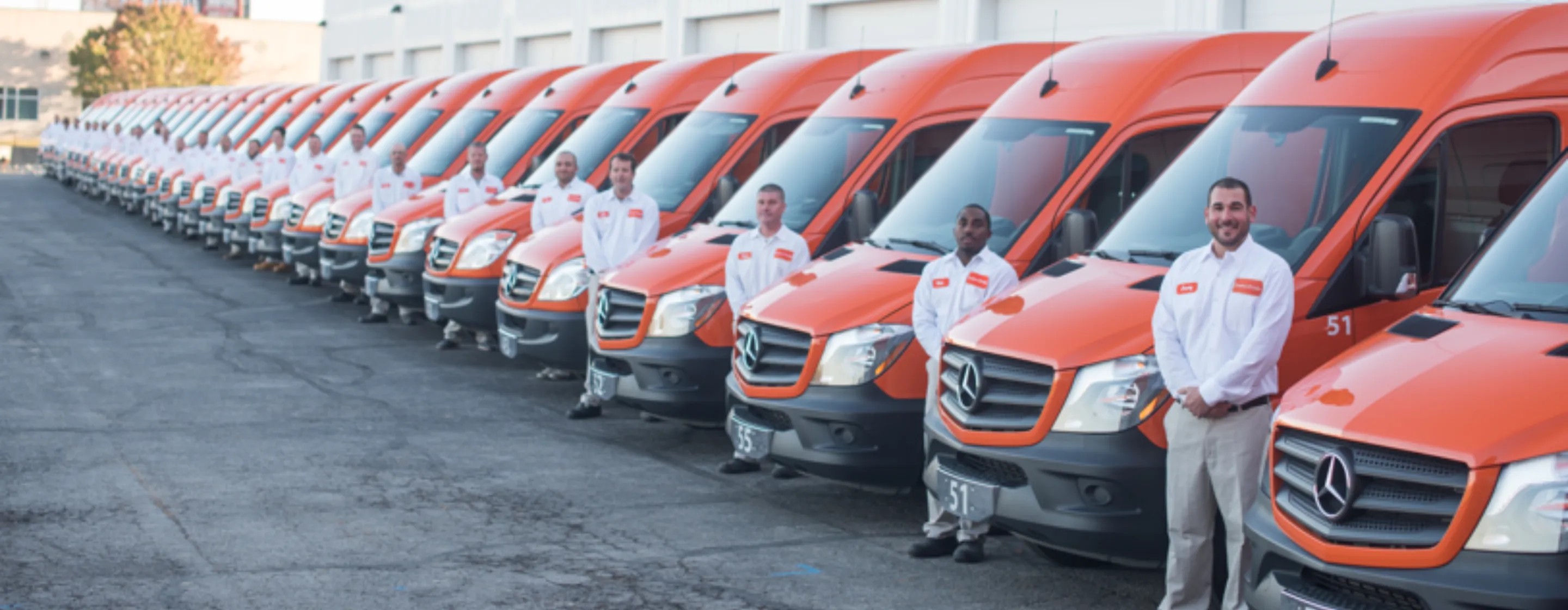 Employees standing next to orange Lawn Pride trucks.