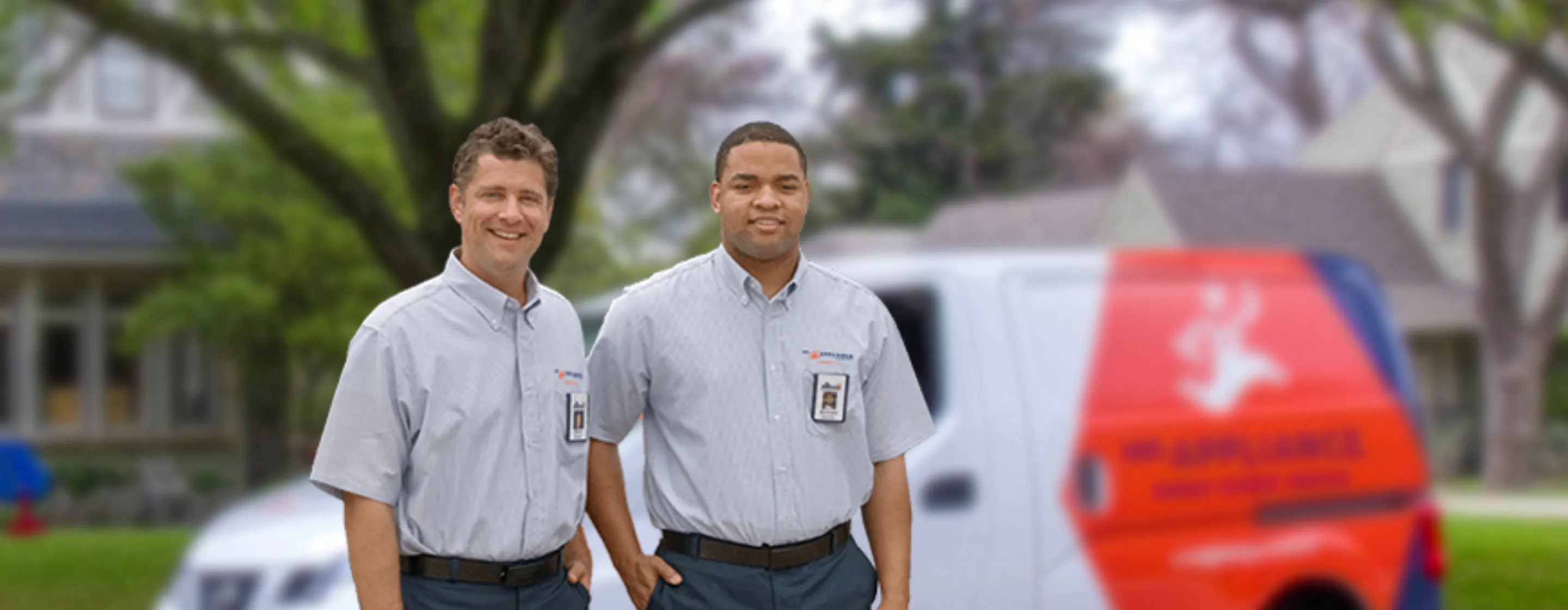 Two male technicians standing in front of a Mr. Appliance branded van.
